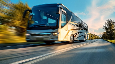 Moderner Reisebus fährt bei Sonnenuntergang dynamisch über eine Landstraße – komfortabel unterwegs mit dem Reisedienst Alkemeyer